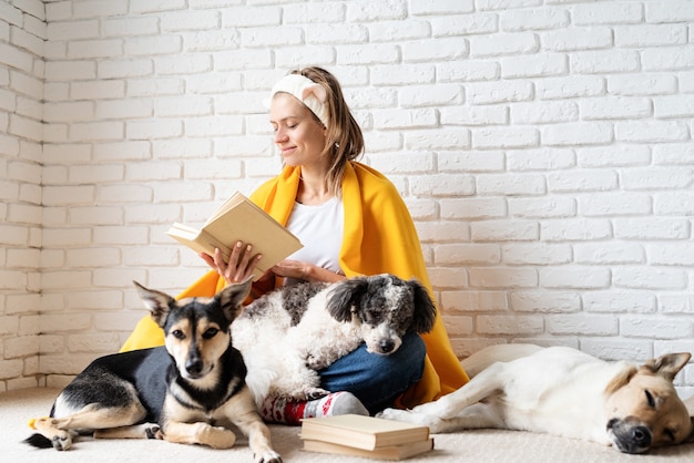 Cuidado de mascotas. Divertida joven sonriente en cuadros amarillos sentada con sus perros leyendo un libro