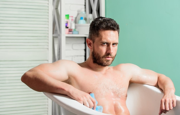 Cuidado masculino. Concepto de sexo y relajación. hombre lavar cuerpo musculoso con esponja de espuma. macho disfrutando del baño. Hombre sexy en el baño. Macho desnudo en la bañera. Lavar la espuma con agua cuidadosamente.