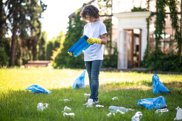 Cuidado del medio ambiente. Teen en blanco thsirt de pie sobre la hierba entre botellas de plástico