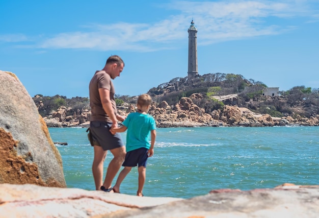 Cuidado de papá Hijo cerca del paseo marítimo pasar tiempo juntos explorar nuevo Hombre sostener la mano del niño Fondo del faro Símbolo de la conciencia individual que eleva la influencia de la unión familiar del padre del niño en la vida del niño feliz