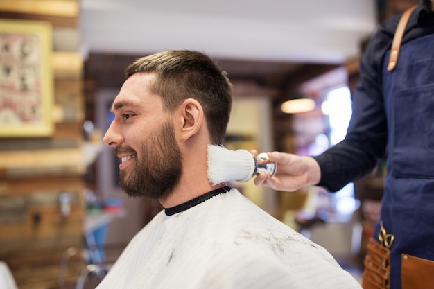 cuidado, peluquería y concepto de personas - hombre y barbero limpiando el cuello con un pincel en la barbería