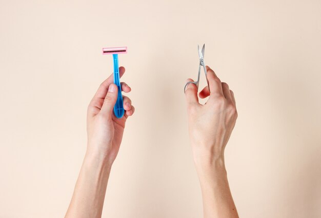 Cuidado personal, concepto de belleza. Manos femeninas sosteniendo un cepillo de dientes y unas tijeras de uñas en beige.