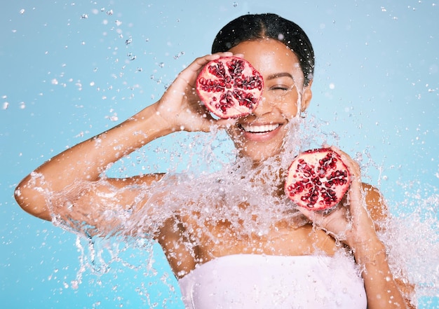 Cuidado de la piel de belleza y mujer con una granada para una piel sana y una dieta sobre un fondo azul Cara de una persona modelo estética con salpicaduras de agua y fruta para una salud y bienestar facial sostenibles