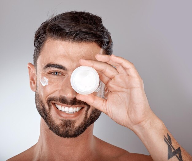 Foto cuidado de la piel de belleza y retrato de hombre con crema sobre fondo gris para tratamiento de spa de bienestar e higiene aseo cosmético y rostro de modelo masculino con autocuidado de loción y tratamiento facial