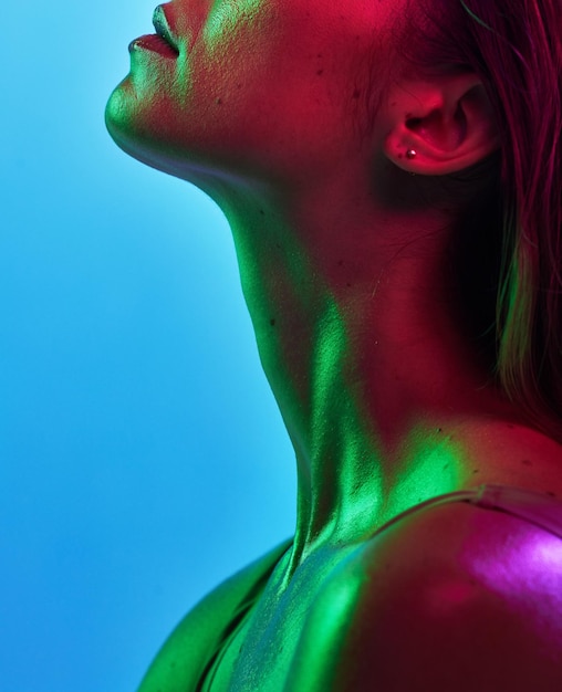 Cuidado de la piel del cuello de la mujer o iluminación de neón sobre un fondo azul aislado en un arte de fantasía moderno o elegante en el estudio Belleza Zoom o brillo corporal modelo en una textura creativa estética de luces verdes o rosas