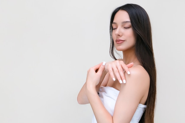 Cuidado de la piel y el cuerpo. Hermosa mujer joven en una toalla toca su piel con las manos.