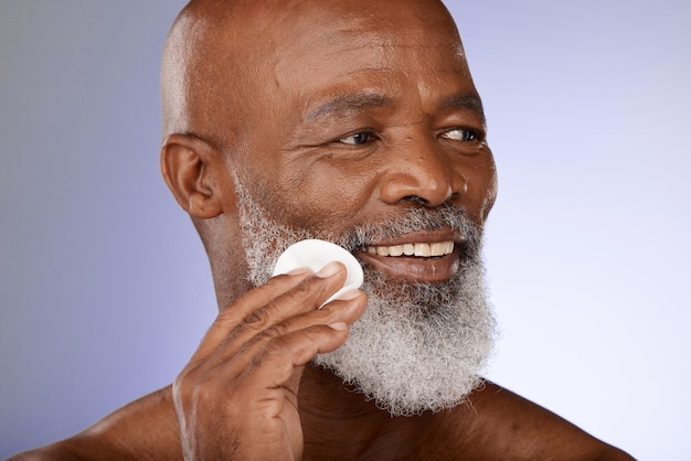 Cuidado de la piel facial y antienvejecimiento con un anciano negro exfoliando su piel en un estudio sobre un fondo gris Limpieza y limpieza de belleza con un hombre maduro que usa una almohadilla de algodón para un tratamiento natural