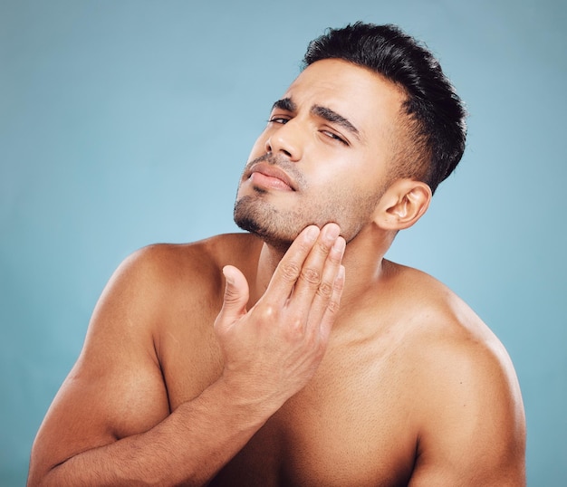 El cuidado de la piel del hombre y los cosméticos táctiles verifican la barba de la piel o el tono de la piel para la salud con el fondo azul del estudio.