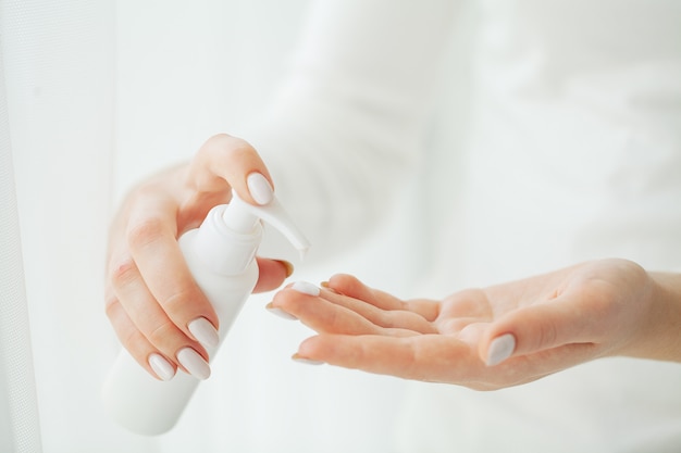 Cuidado de la piel de las manos. Cerca de manos femeninas con tubo de crema, manos de mujer hermosa con uñas de manicura natural aplicando crema cosmética para manos sobre piel suave, sedosa y saludable