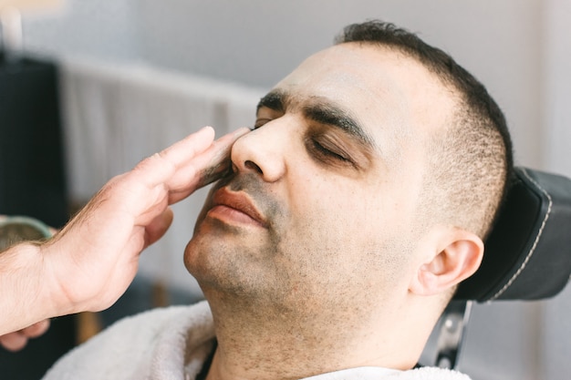 Cuidado de la piel masculina en un salón de belleza. aplicando mascarilla limpiadora de arcilla en la cara de un hombre