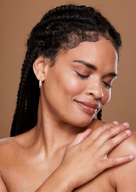 Cuidado de la piel de mujer negra y cara con sonrisa en relajación para cosméticos o maquillaje contra un fondo de estudio marrón Mujer afroamericana tocando el hombro en satisfacción por un tratamiento de piel de belleza suave