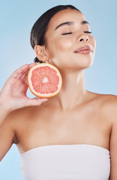 Cuidado de la piel de la mujer de toronja y fruta de bienestar para el cuidado de la cara bienestar y salud de la dieta sobre un fondo azul en el estudio Sonrisa feliz y modelo brasileño de belleza con productos alimenticios de vitamina c en las manos