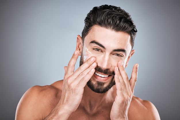 Foto cuidado de la piel de retrato facial y hombre con crema en estudio aislado en un fondo gris para el bienestar facial dermatología cosmética o modelo masculino feliz con crema de loción o producto humectante para la salud