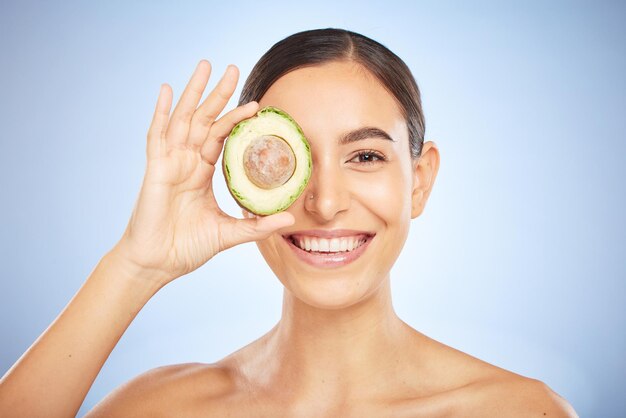 Cuidado de la piel de retrato facial y mujer con aguacate aislado en un fondo de estudio azul Cosméticos de belleza y modelo femenino joven con alimentos de frutas o productos para la nutrición grasas saludables y vitamina c