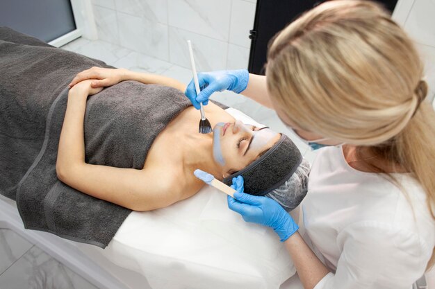 Cuidado profesional de la piel en clínica de cosmetología médico dermatólogo aplica crema con cepillo