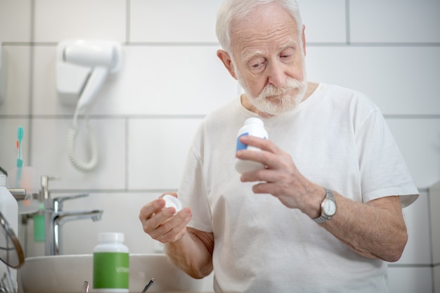 Cuidado de la salud. Hombre canoso en camiseta blanca con botellas de vitaminas en sus manos