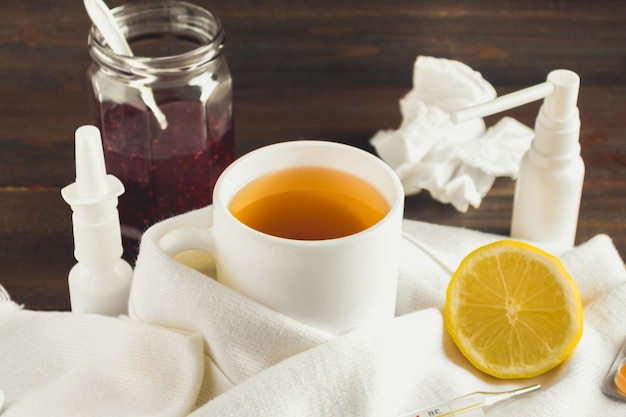 Cuidado de la salud medicina tradicional y concepto de gripe taza de té con termómetro de limón y medicamentos en la mesa de madera