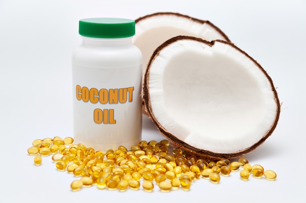 Cuidado de la salud Suplemento nutricional Botella de aceite de coco con coco partido a la mitad en el costado y cápsula de gel de oro dispersa en la parte delantera Aislado en la superficie blanca