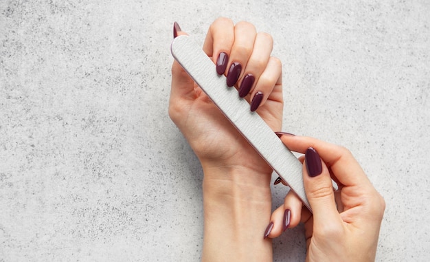 El cuidado de las uñas con una lima de uñas para lograr una manicura perfecta en casa en una encimera gris