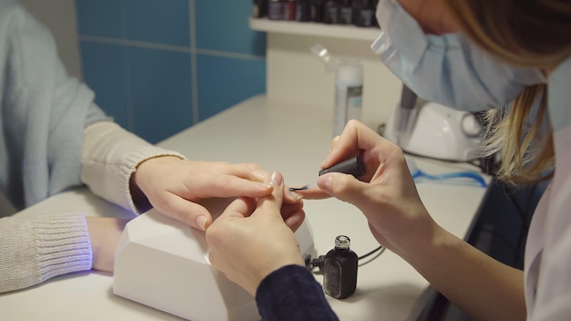 El cuidado de las uñas en el maestro del salón aplica gelacquer en las uñas de una mujer joven