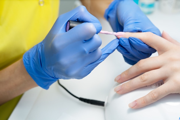 Cuidado de uñas. Manicura en el salón. El maestro manicura a la niña, belleza y salud. Proceso de manicura. Máster en máscara y guantes. Esmalte de uñas.