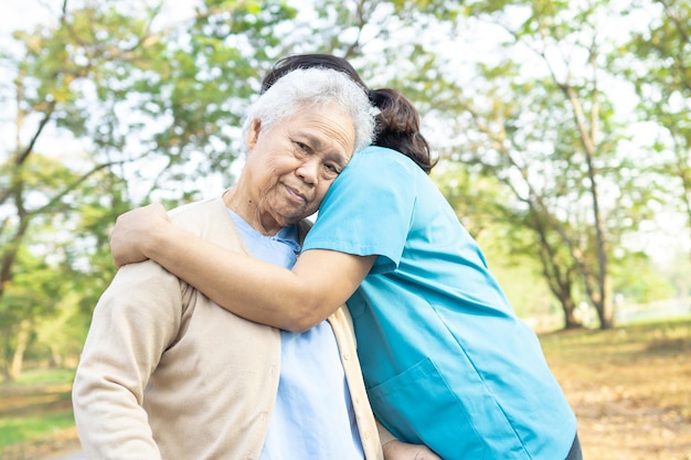 El cuidador abraza y ayuda a la mujer mayor asiática en el parque concepto médico fuerte y saludable