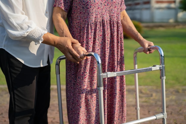 Cuidador ajuda paciente idosa asiática a andar com caminhante no conceito médico forte e saudável do parque