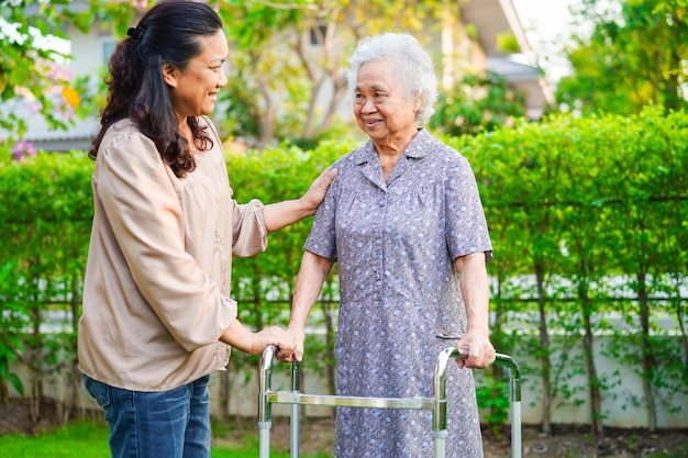 Cuidador ajuda paciente idosa asiática com deficiência a andar com caminhante no conceito médico do parque
