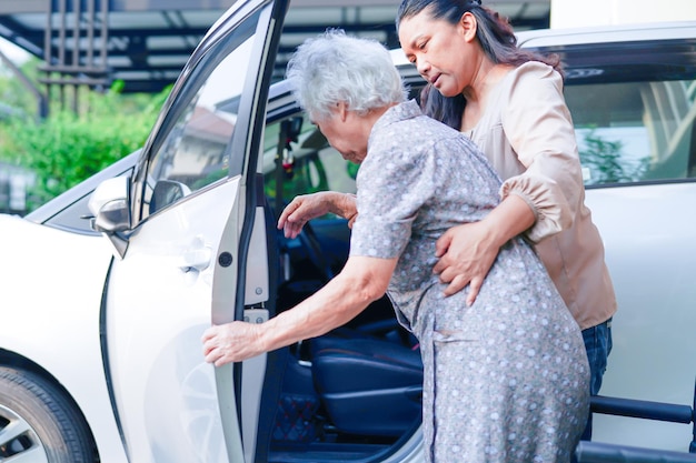 Cuidador ajuda paciente idosa asiática com deficiência a entrar em seu conceito médico de carro