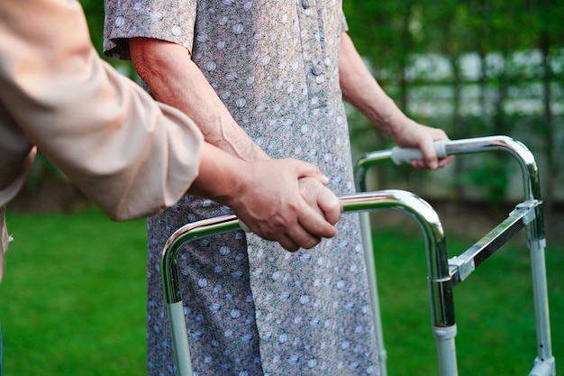 Cuidador ajuda paciente idosa asiática com deficiência andar com andador no conceito médico do hospital de enfermagem