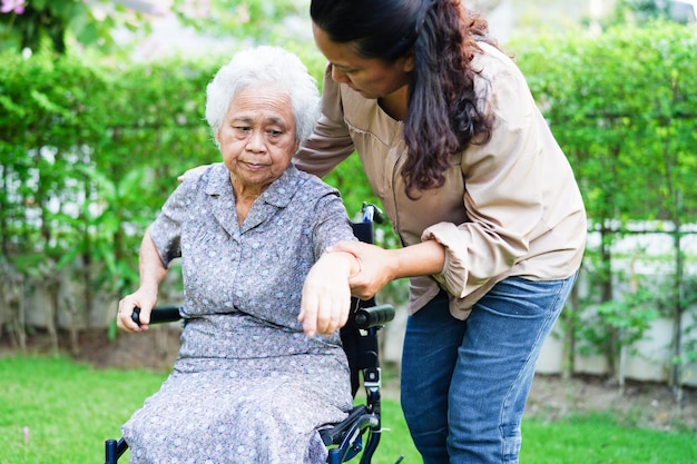 Cuidador ajuda paciente idosa asiática com deficiência sentada em cadeira de rodas no conceito médico do parque
