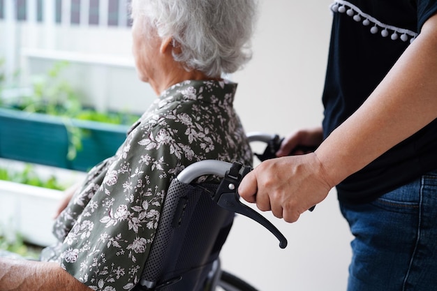 Cuidador ajuda paciente idosa asiática com deficiência sentada em cadeira de rodas no conceito médico hospitalar