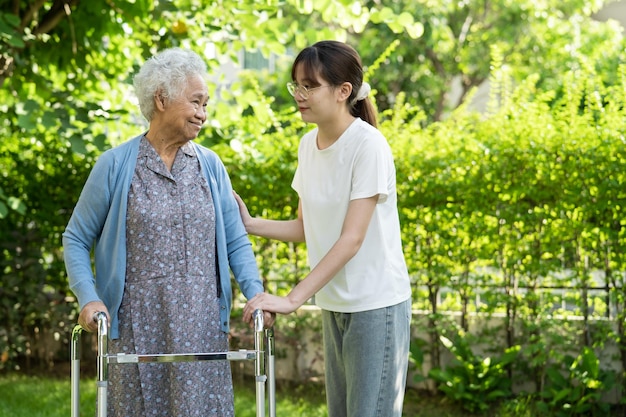 Cuidador ajudar asiática idosa mulher paciente caminhar com caminhante no parque saudável forte conceito médico