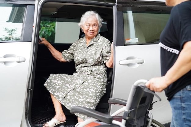 El cuidador ayuda a una anciana asiática con discapacidad a entrar en el concepto médico de su automóvil