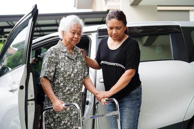 El cuidador ayuda a una anciana asiática con discapacidad a entrar en el concepto médico de su automóvil
