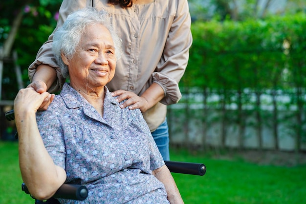 El cuidador ayuda a una anciana asiática con discapacidad a una paciente sentada en silla de ruedas en el concepto médico del parque