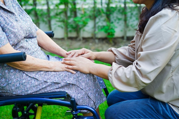 El cuidador ayuda a una anciana asiática con discapacidad a una paciente sentada en silla de ruedas en el concepto médico del parque