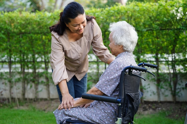 El cuidador ayuda a una anciana asiática con discapacidad a una paciente sentada en silla de ruedas en el concepto médico del parque