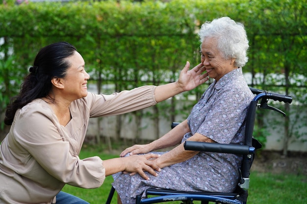 El cuidador ayuda a una anciana asiática con discapacidad a una paciente sentada en silla de ruedas en el concepto médico del parque