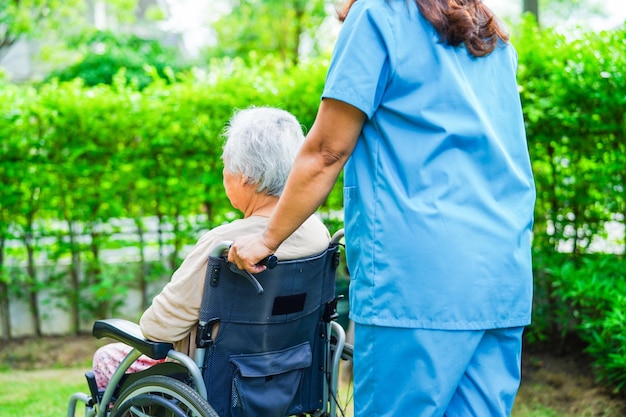 El cuidador ayuda a una anciana asiática con discapacidad a una paciente sentada en silla de ruedas en el concepto médico del parque