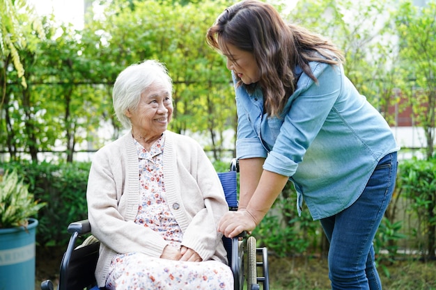 Foto el cuidador ayuda a una anciana asiática con discapacidad sentada en silla de ruedas en el concepto médico del parque