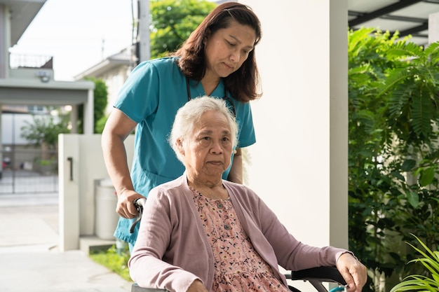 El cuidador ayuda a una anciana asiática sentada en una silla de ruedas