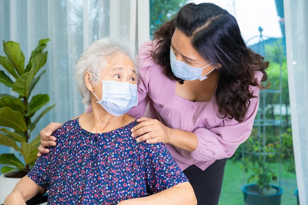 El cuidador ayuda a una anciana o anciana asiática sentada en silla de ruedas y usando una máscara facial para proteger la infección de seguridad Covid19 Coronavirus