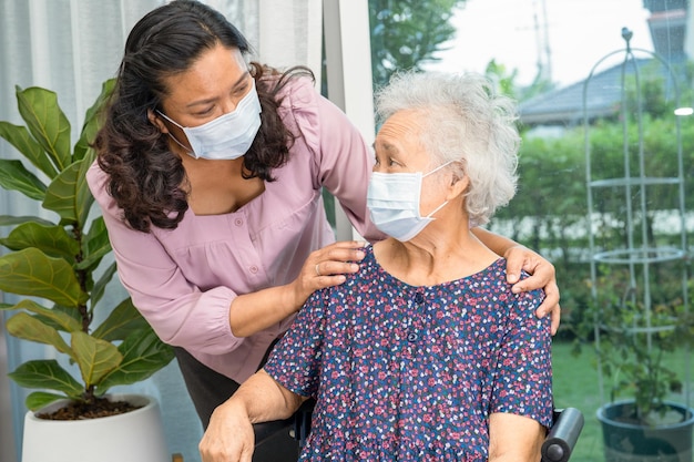 El cuidador ayuda a una anciana o anciana asiática sentada en silla de ruedas y usando una máscara facial para proteger la infección de seguridad Covid19 Coronavirus