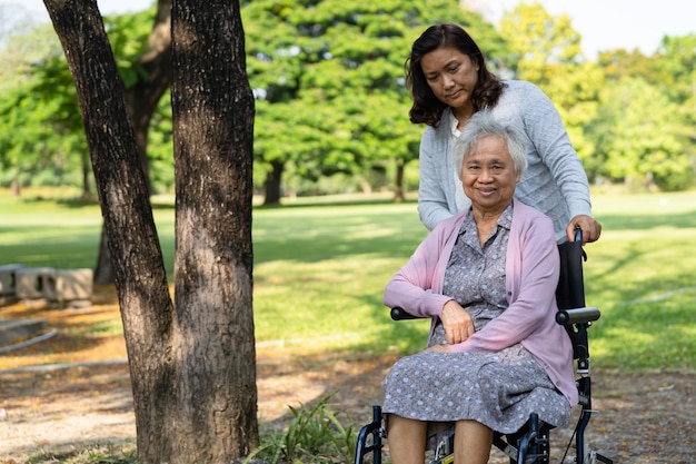 El cuidador ayuda y cuida a una anciana asiática que usa un andador con buena salud mientras camina en el parque en felices vacaciones frescas