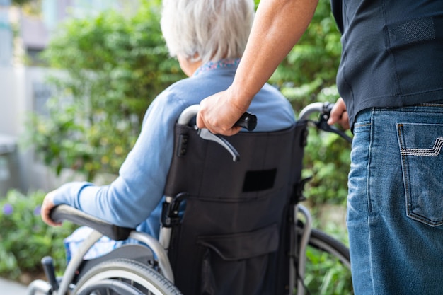 Cuidador ayuda y cuida a una anciana asiática sentada en silla de ruedas para ir a la rampa en un hospital de enfermería concepto médico fuerte y saludable