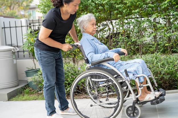 Cuidador ayuda y cuida a una anciana asiática sentada en silla de ruedas para ir a la rampa en un hospital de enfermería concepto médico fuerte y saludable