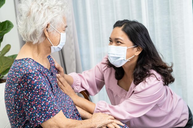 El cuidador ayuda y habla con una anciana asiática o una anciana que usa una máscara facial para proteger la infección de seguridad Covid19 Coronavirus en el parque