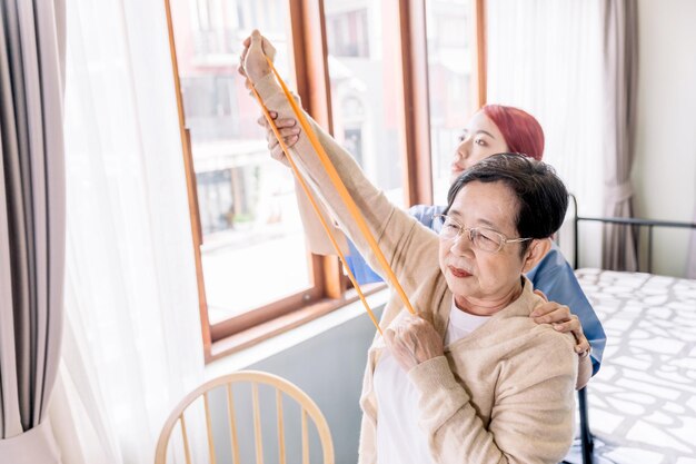 Cuidador de enfermeira usando exercícios de esfrega com uma mulher asiática sênior usando exercícios de banda de resistência para o paciente sênior em tratamento de fisioterapia Cuidados de saúde em casa e conceito de lar de idosos