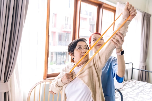 Cuidador de enfermeira usando exercícios de esfrega com uma mulher asiática sênior usando exercícios de banda de resistência para o paciente sênior em tratamento de fisioterapia Cuidados de saúde em casa e conceito de lar de idosos